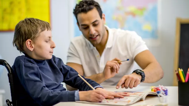 Child in a wheelchair painting at a desk with a paraprofessional